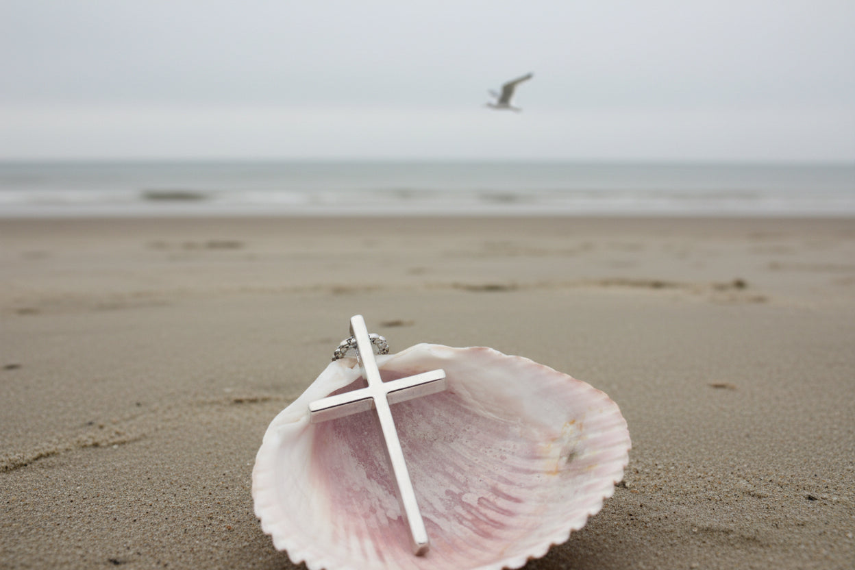 Silver cross pendant on a shell with a natural background