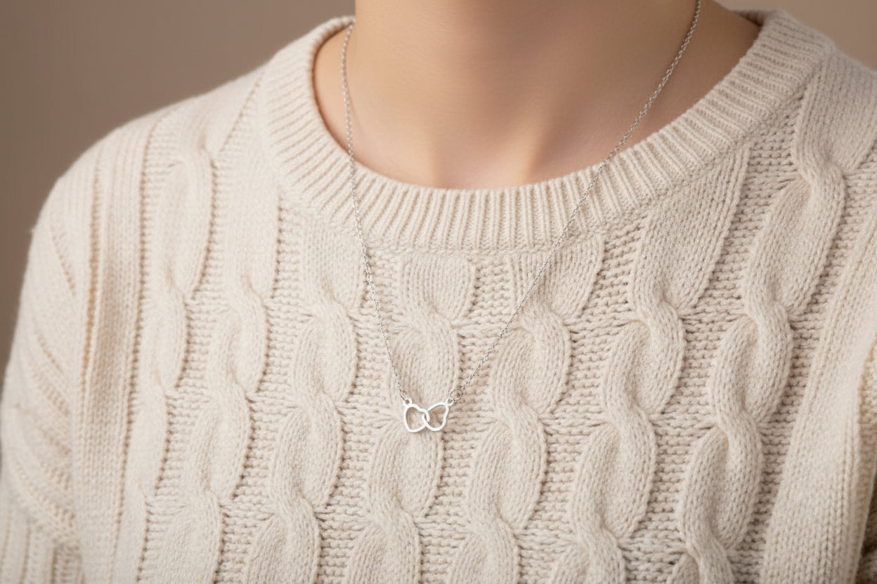 Silver necklace on a black display card with a hand holding it