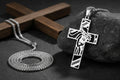 Silver cross pendant with Jesus Christ's face on a dark surface