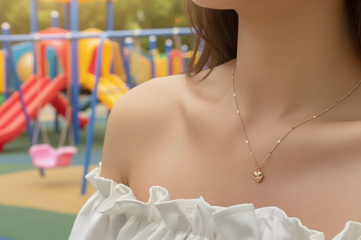 Gold necklace with a heart pendant on a person wearing a white top.